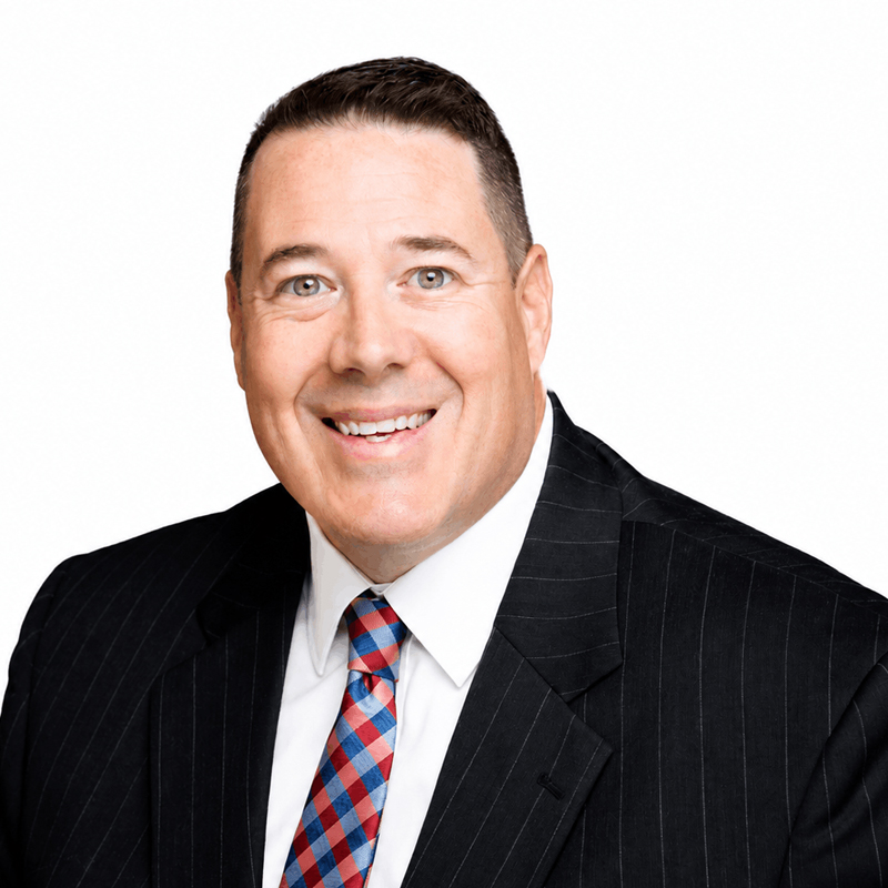 Smiling man in a dark pinstripe suit and red-blue tie, close-up portrait against a white background.
