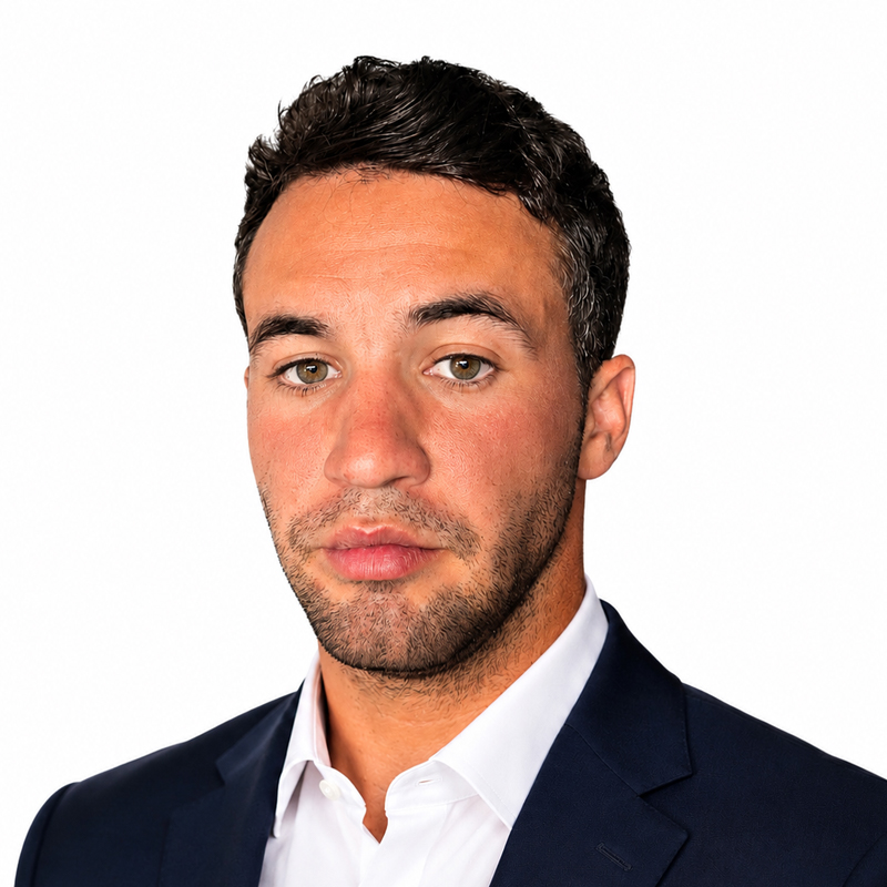 Professional headshot of a man in a navy suit and white shirt, looking at the camera on a white background.